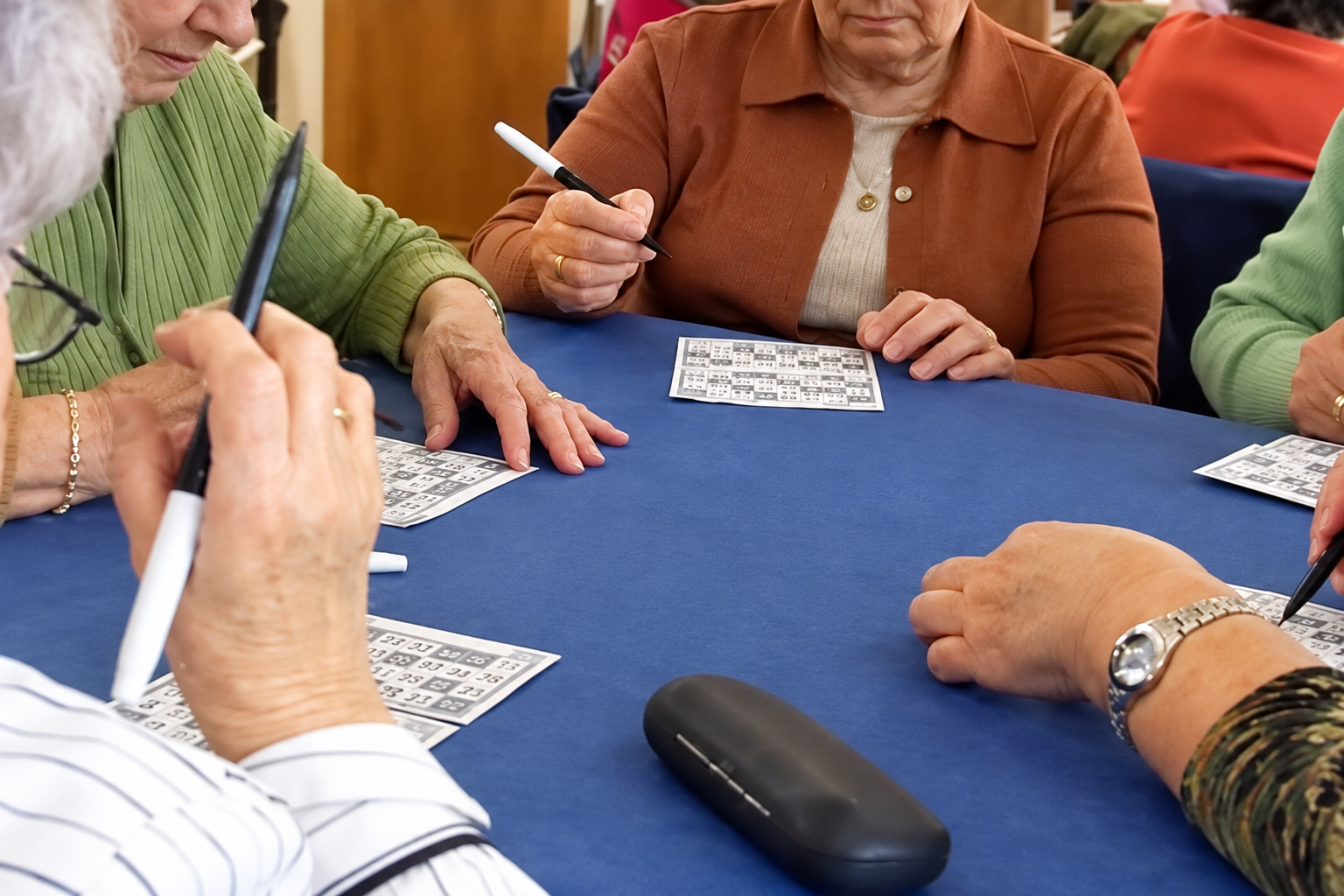 Personas mayores comparten una partida de bingo con cartones y rotuladores alrededor de una mesa
